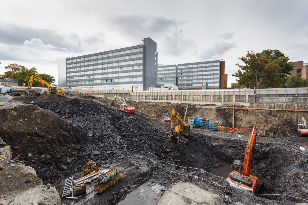 Urban construction site with excavators digging a large pit.