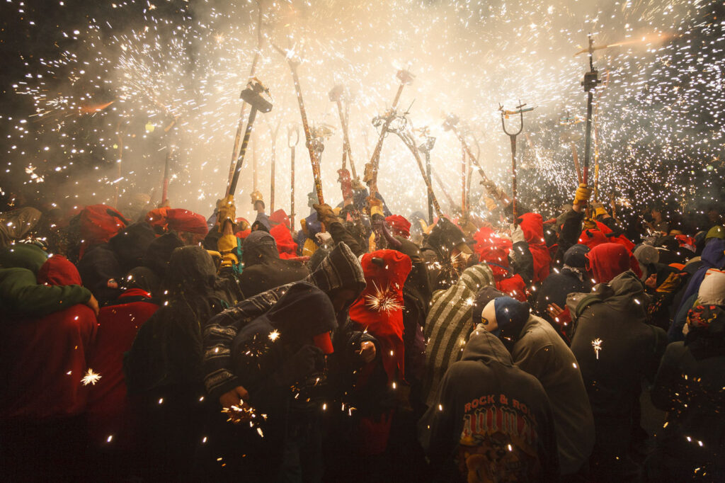 Vibrant night festival with people, sparks, and pyrotechnics.