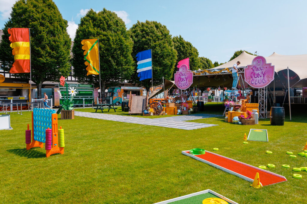 Vibrant outdoor festival with games, food trucks, and Pink Pony Club.