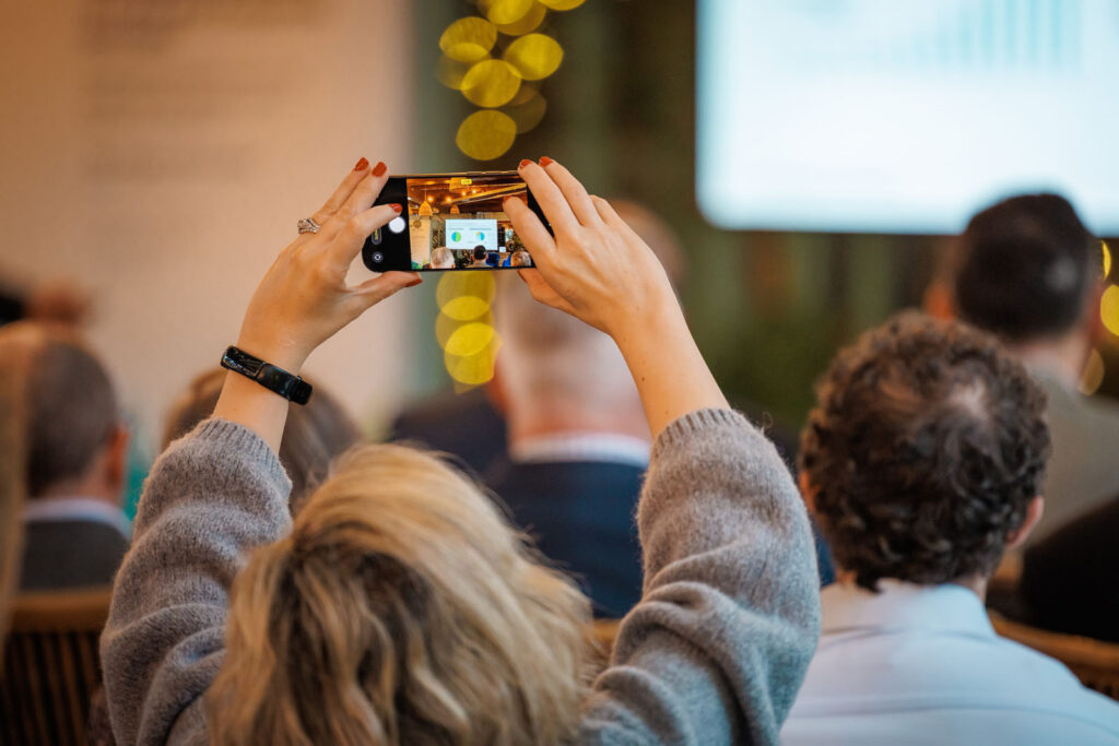 Woman captures presentation on smartphone.