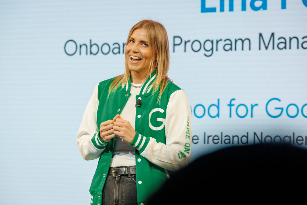 Woman in green jacket speaks on stage at Google event.