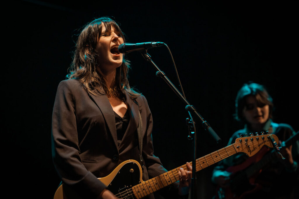 Woman sings and plays guitar live on stage.