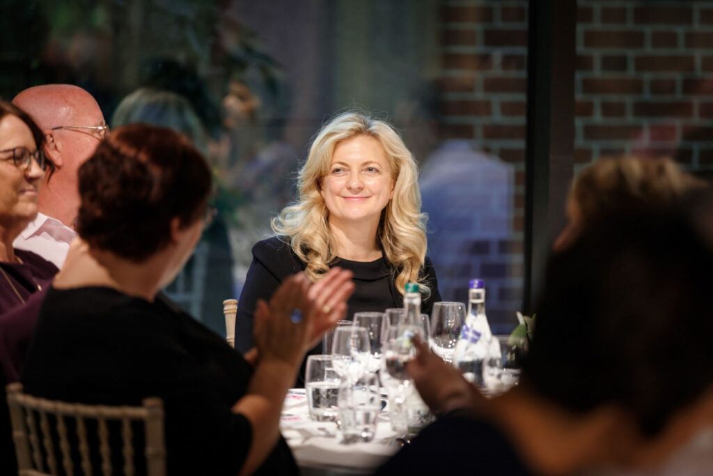 Woman smiling at a table, people clapping.
