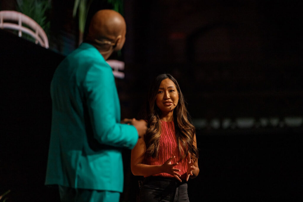 Woman speaker engaging with man on dark stage.