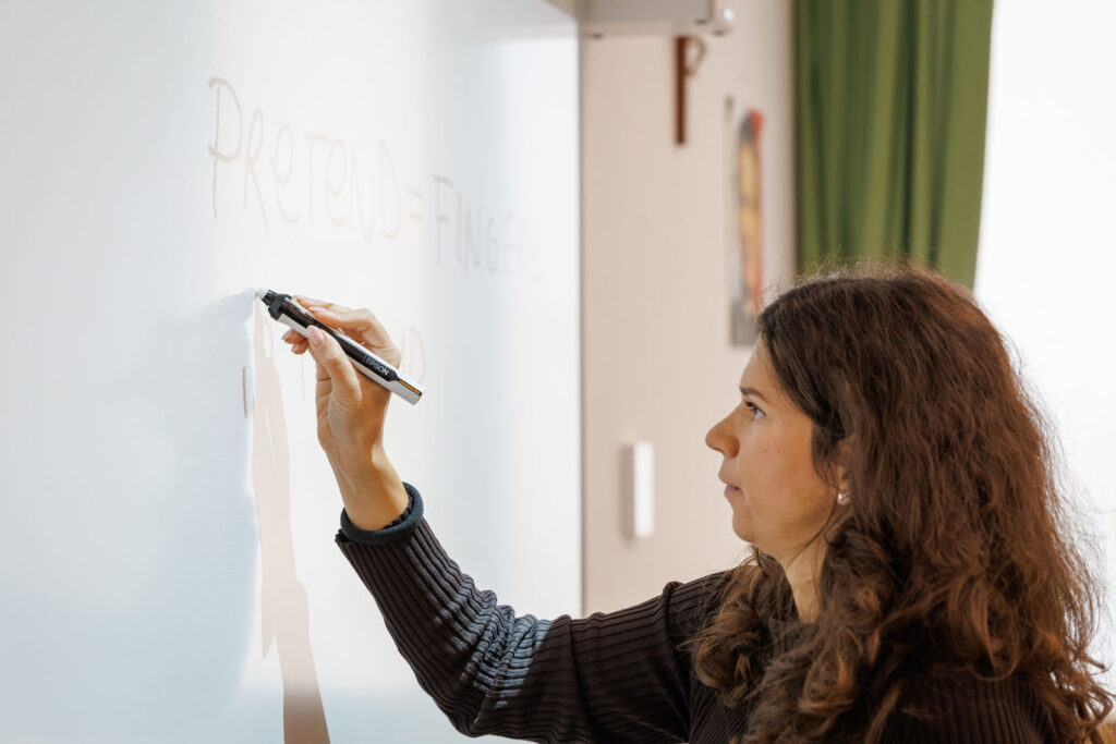 Woman writing "PRETEND" on a whiteboard.