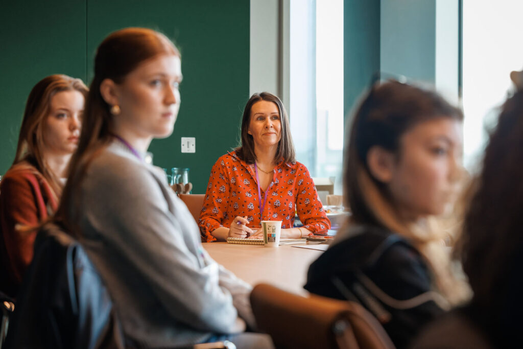 Women in a meeting, one woman in red shirt smiling.