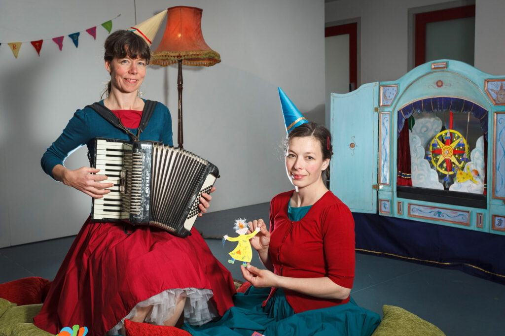 Women in party hats with accordion and puppet theater.