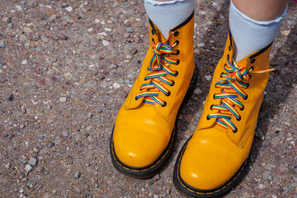 Yellow boots with rainbow laces on gravel.